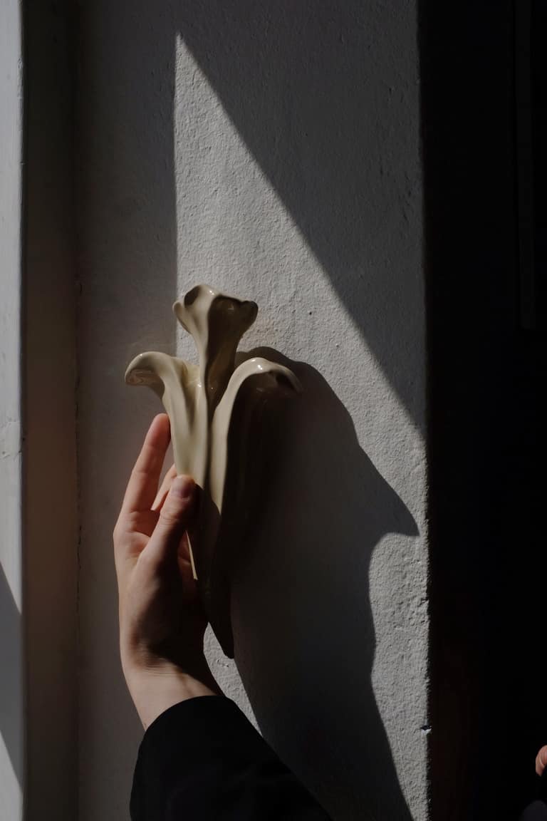 A hand holding an abstract ceramic sculpture against a sunlit wall.