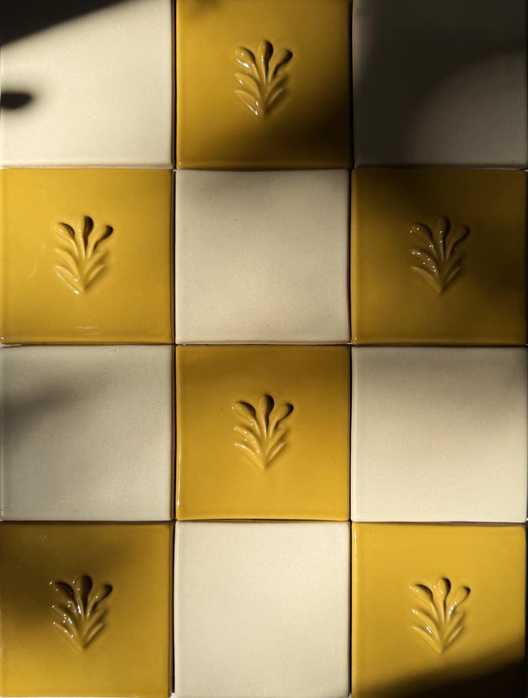 Close-up of yellow and white ceramic tiles featuring embossed leaf patterns, arranged in a grid with dramatic lighting.