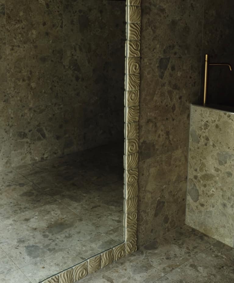 A corner view of a bathroom featuring textured stone tiles and a decorative swirled border.