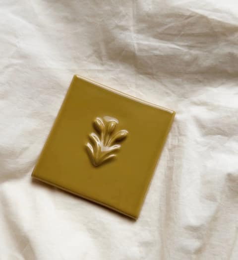 A single relief tile in glossy ochre glaze on linen