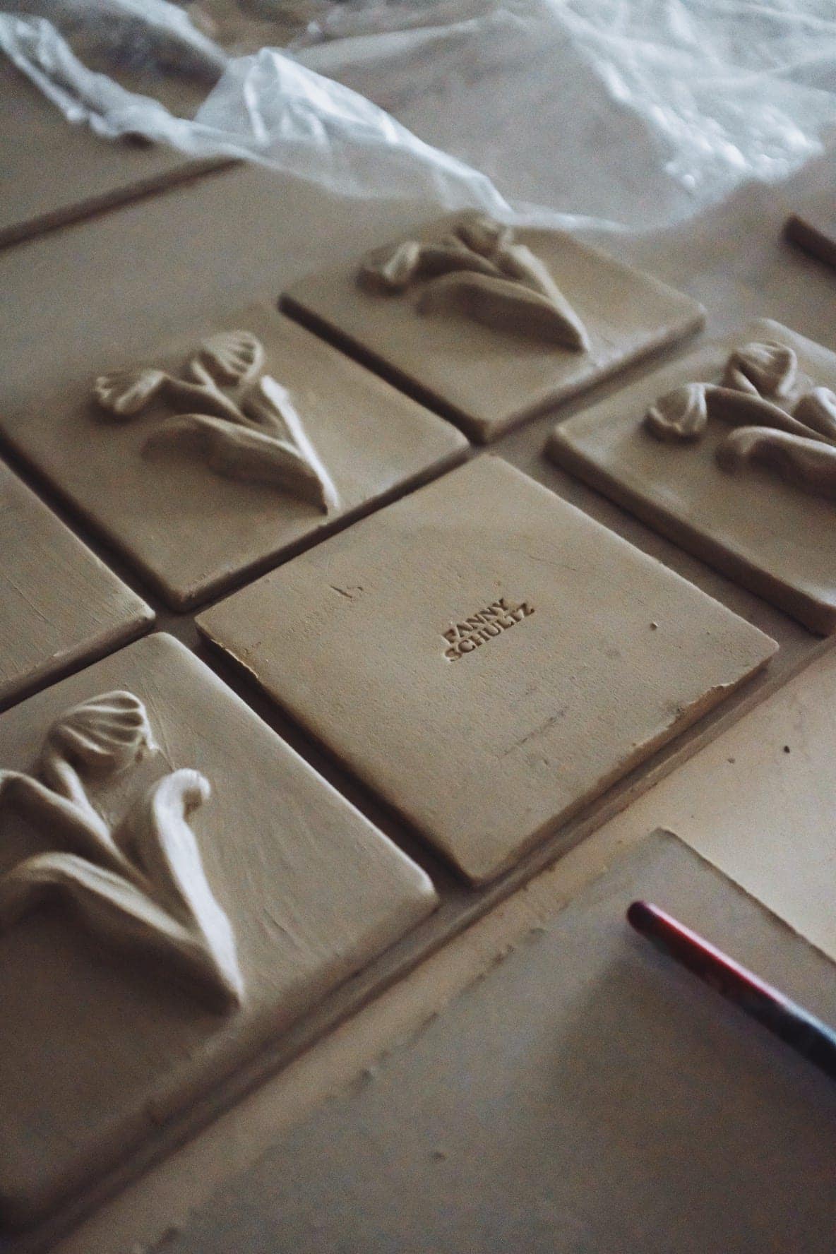 Unfired tiles laid out in the studio, one stamped Fanny Schultz