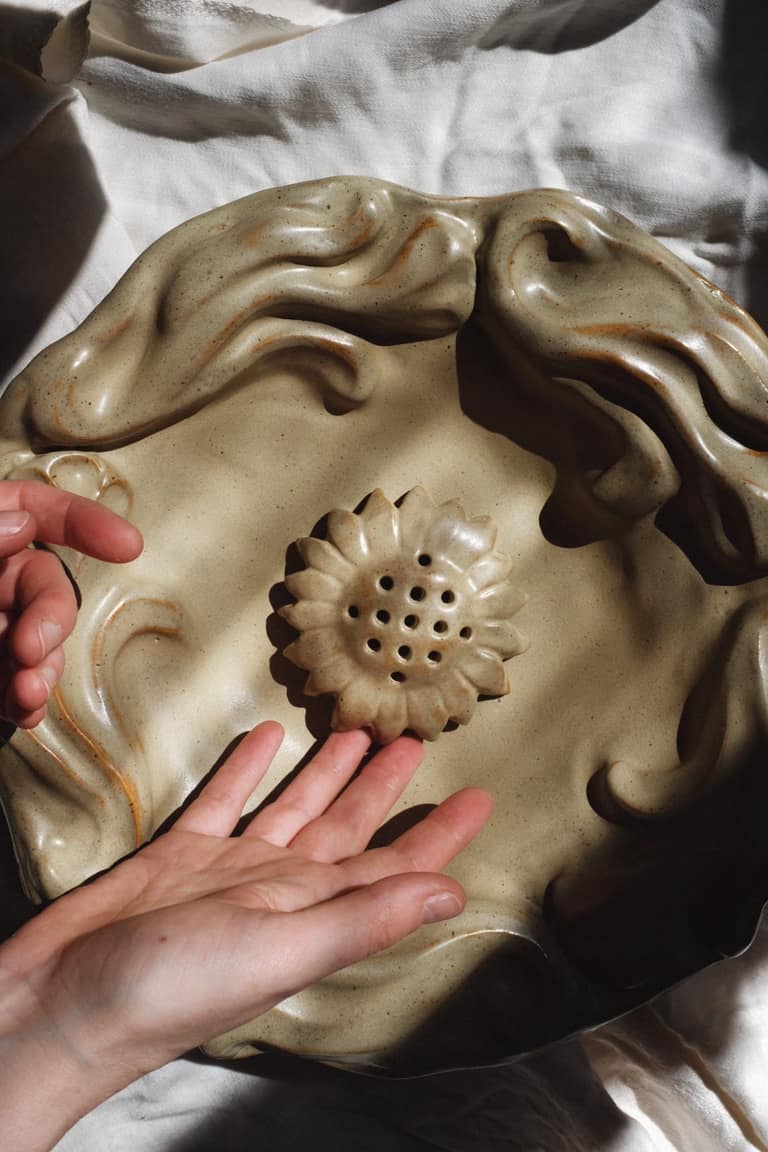 Hands resting on the Floral Tray in beige glaze, a pierced sunflower at its centre