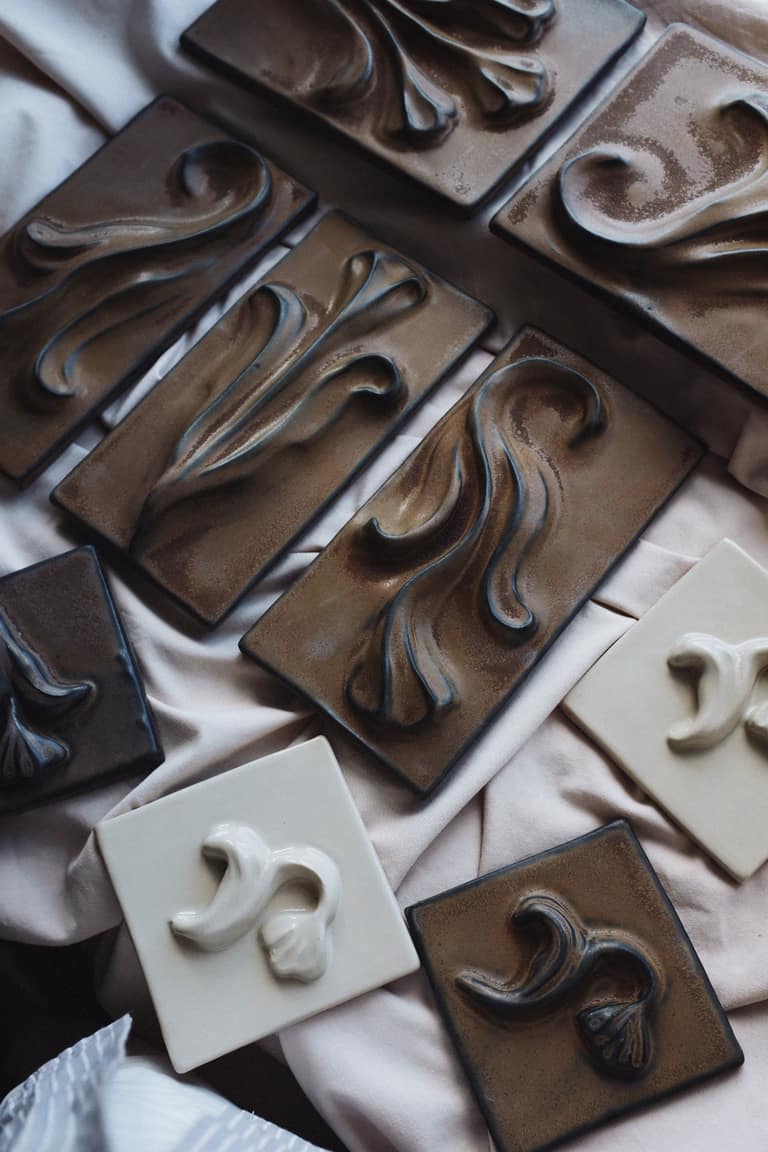 A collection of rectangular ceramic tiles in brown and cream glazes featuring raised relief designs of stylized leaves.